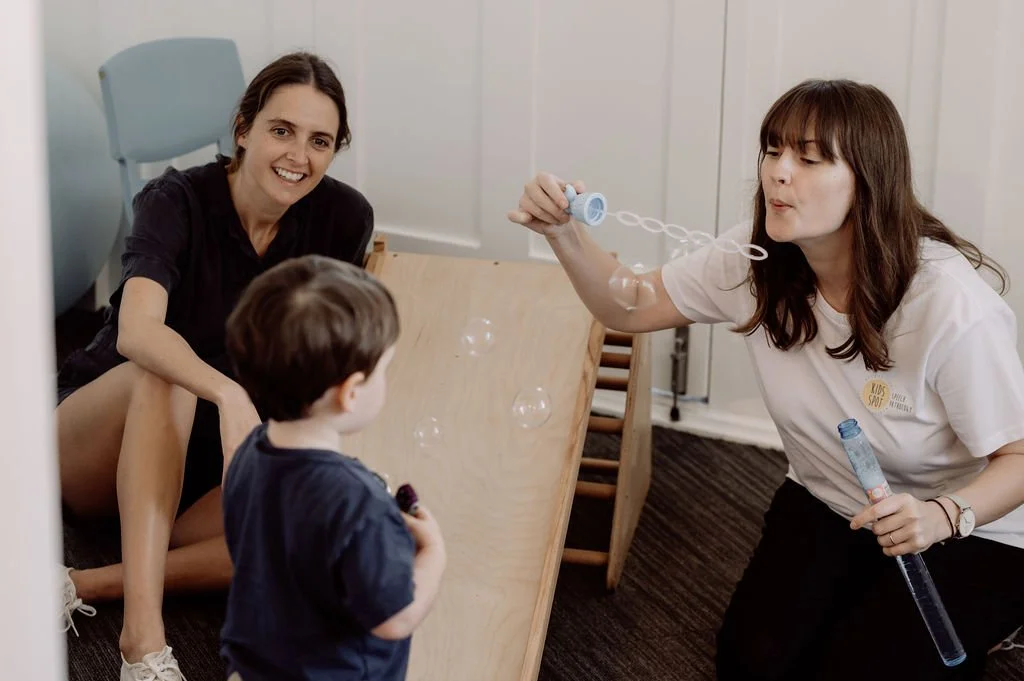 Julia blowing bubbles during a session with a child and parent at Kids Spot